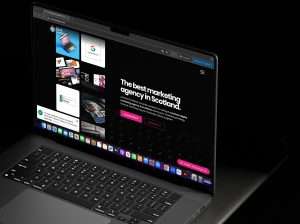 A laptop screen displays a marketing agency website with a header proclaiming "The best marketing agency in Scotland," showcasing innovative trends and offering options to view their work and contact them.