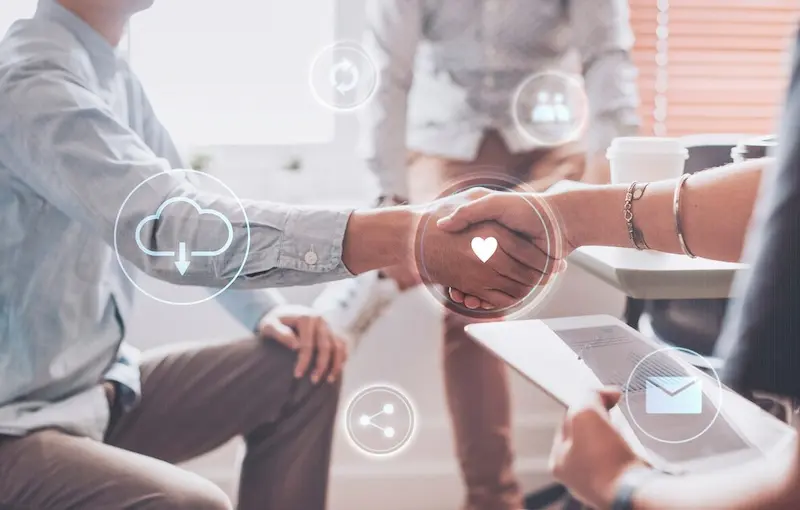 In an Inverness office setting, two people shake hands as a myriad of digital icons, including cloud, heart, and email symbols, overlay their interaction—an emblem of collaboration.