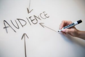 A close-up of a person writing the word "Audience" in black pen surrounded by arrows on a whiteboard